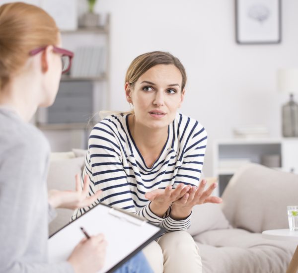 Red haired psychiatrist listening her patient after traumatic events while sitting on beige settee